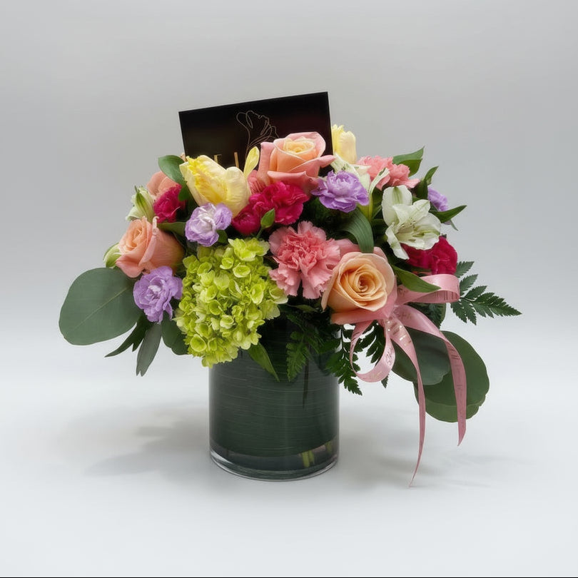 Colorful bouquet of flowers in a vase with a pink gift bag in the background.
