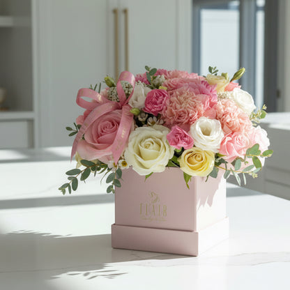 Floral arrangement in a decorative box on a white surface with a blurred background