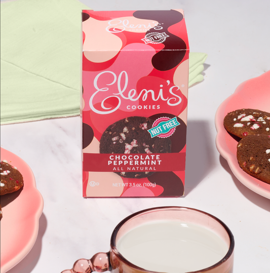 Box of Eleni's Chocolate Peppermint Cookies with cookies and a glass of milk on a white background