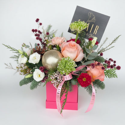 Floral Holiday arrangement with a pink box and gold ornament with white background