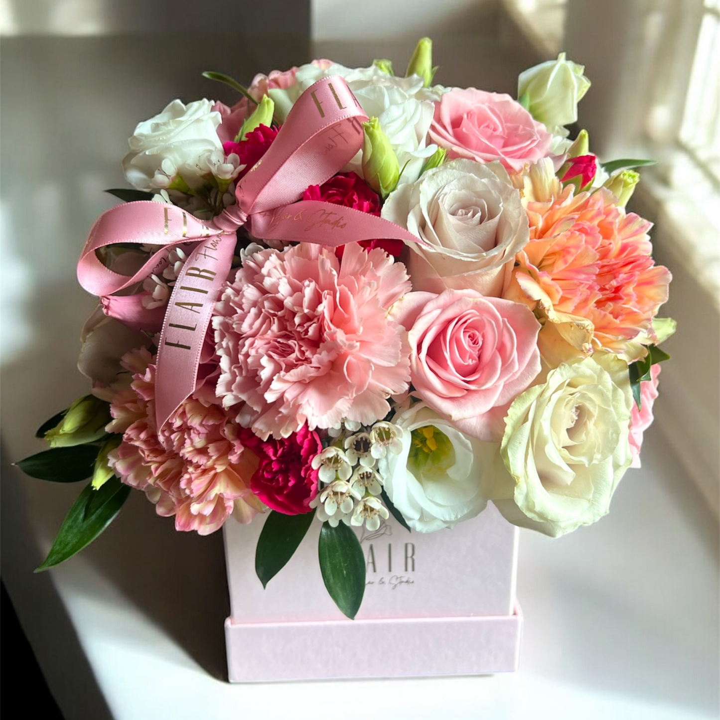 Floral arrangement with pink ribbon in a box on a light background