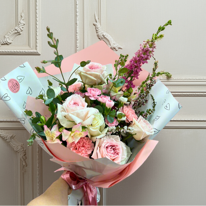 Bouquet of flowers with pink and white wrapping paper against a light gray wall.