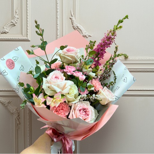Bouquet of flowers with pink and white wrapping paper against a light gray wall.