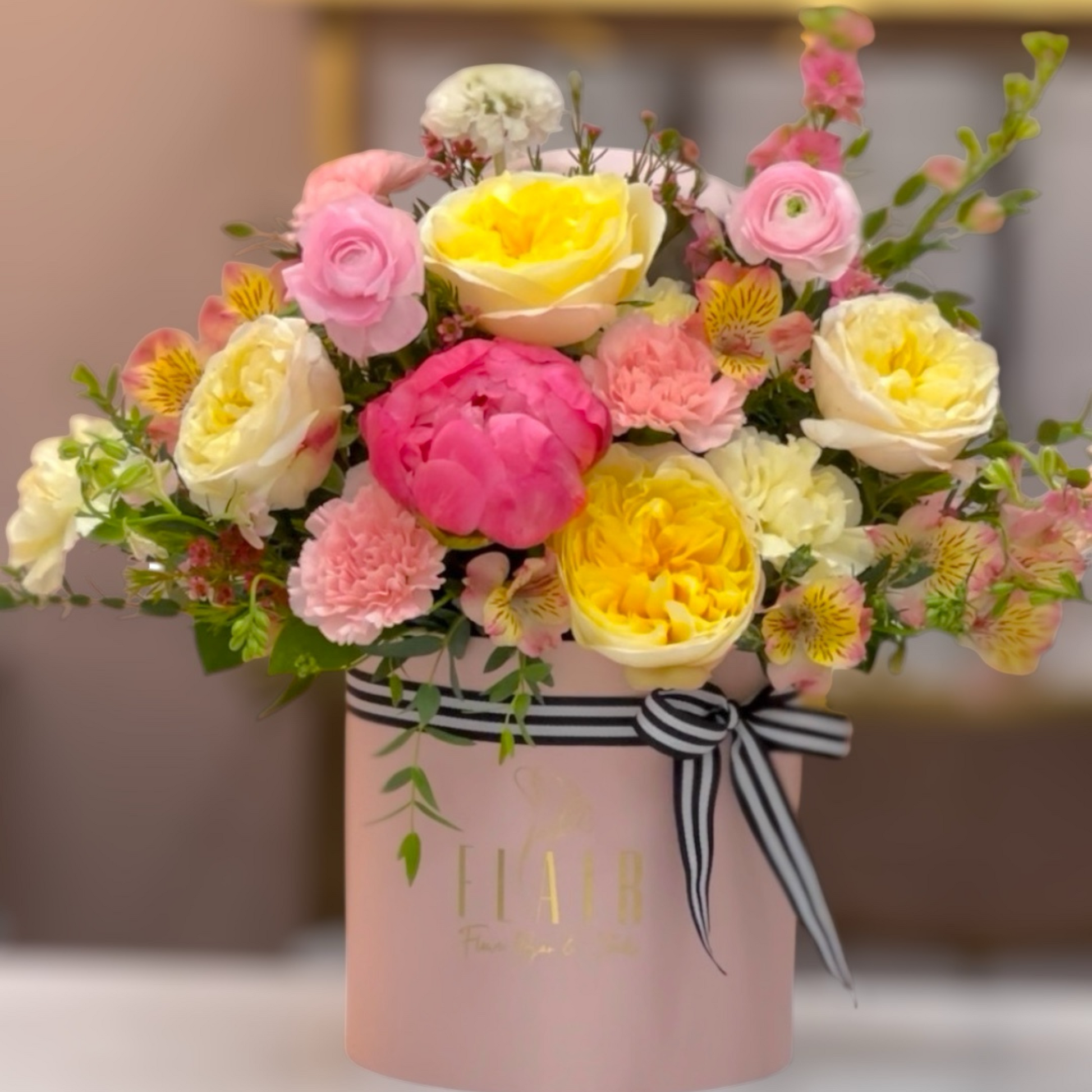 Bouquet of flowers in a pink box with a black and white ribbon on a blurred background