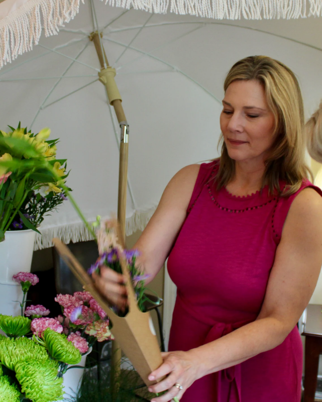 Woman in a pink dress arranging flowers under an umbrella- Flower Bar Rental_Cincinnati_Northern Kentucky