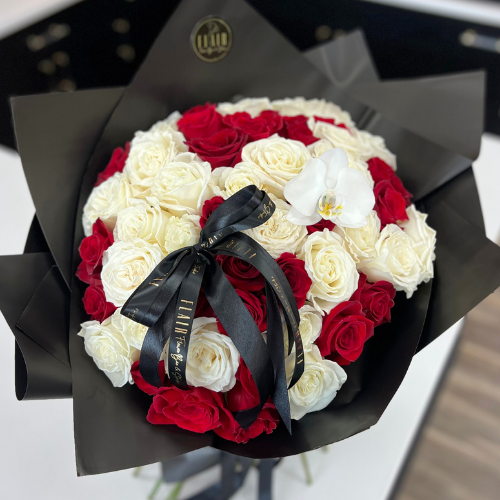 Bouquet of red and white roses with a black ribbon, wrapped in black paper, on a blurred background.