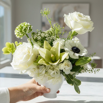 Bouquet of white and green flowers in a white vase held by a hand by Flair Flower Bar