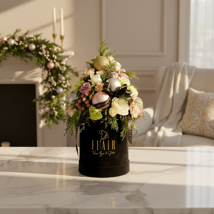 Decorative floral arrangement in a black velvet container on a marble surface with a festive wreath in the background.