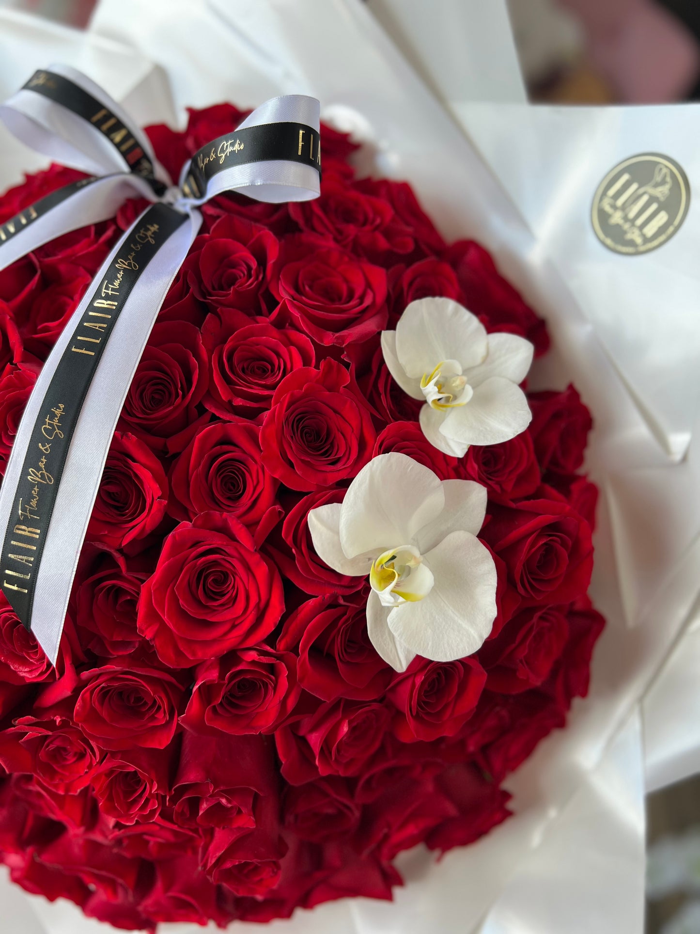 Bouquet of red roses with white orchids and a gold ribbon on a white background
