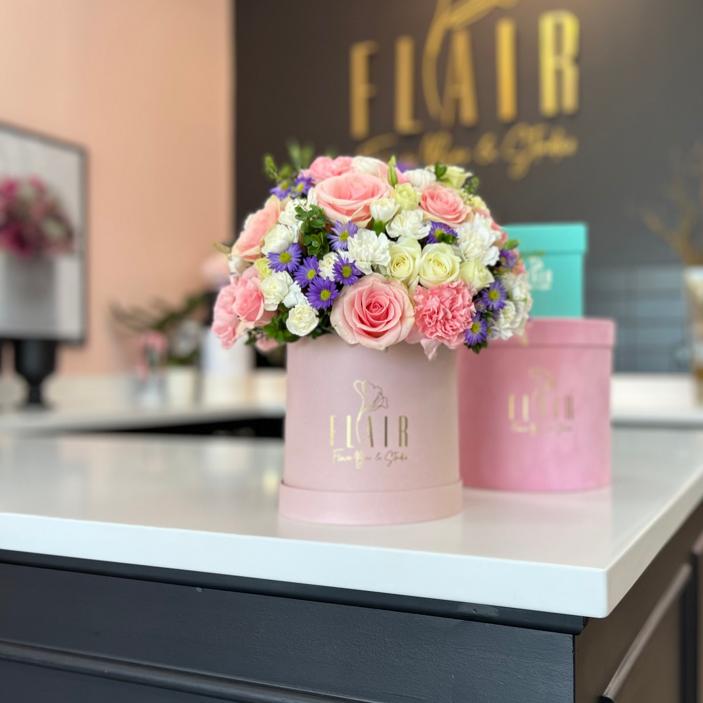 Floral arrangement in a pink box on a counter with 'FLAIR' branding in the background.