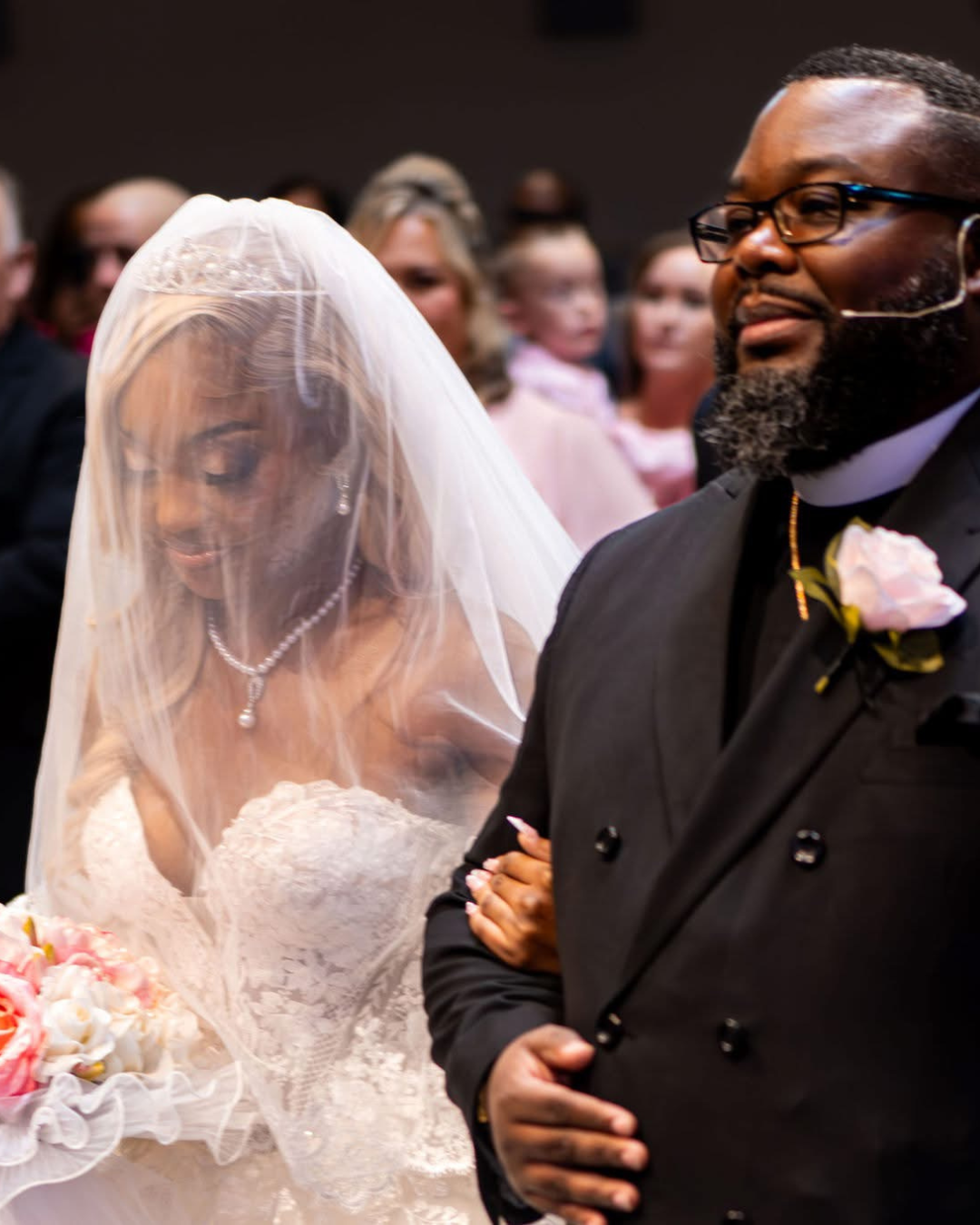 Man in a suit with a woman in a wedding dress and veil, surrounded by people. Wedding Pink Flowers - Florence, Kentucky 