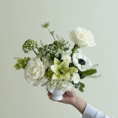 Bouquet of white and green flowers held by a hand against a light background