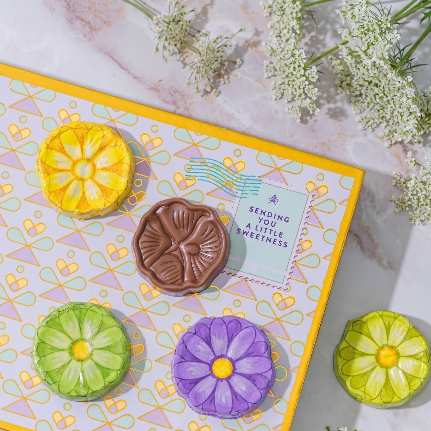 Colorful flower-shaped cookies on a decorative box with a card inside, surrounded by flowers.