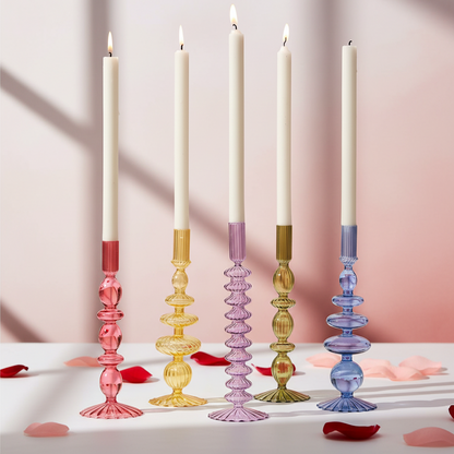 Colorful glass candle holders with candles on a soft pink background