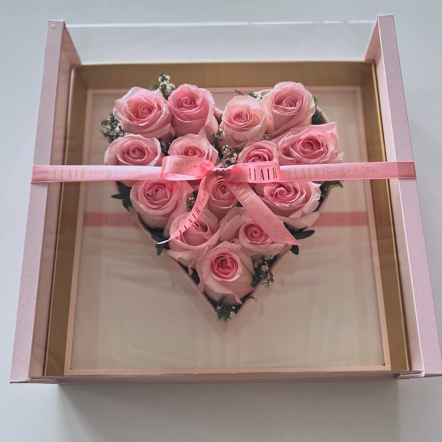 Heart-shaped arrangement of pink roses in a box with a pink ribbon on a light gray background for Cincinnati delivery from Flair Flower Bar