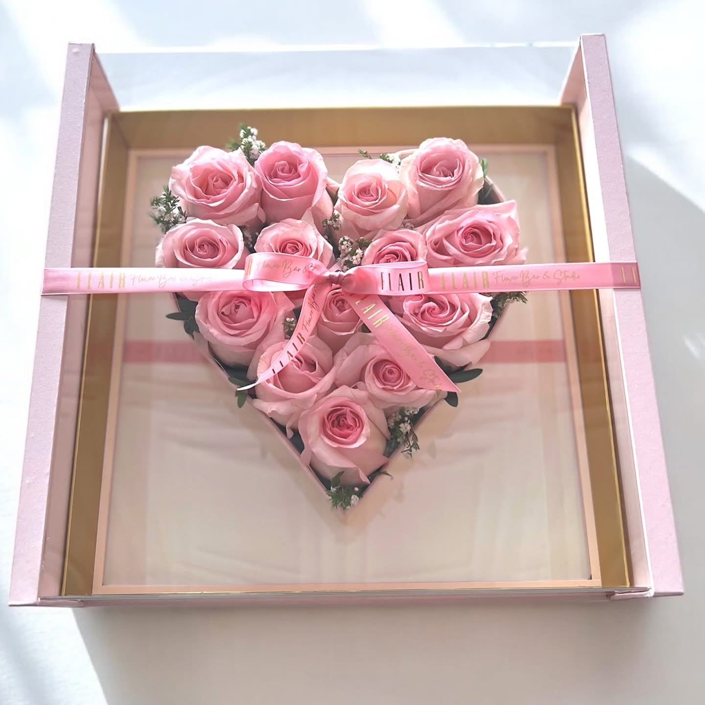 Heart-shaped arrangement of pink roses in a box with a pink ribbon on a white background for delivery to Cincinnati and Northern Kentucky from Flair Flower Bar