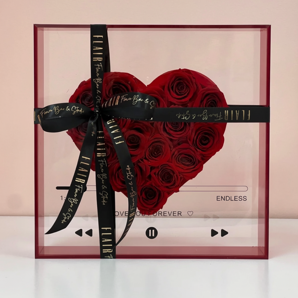 Heart-shaped arrangement of preserved red roses with a black ribbon on a pink background