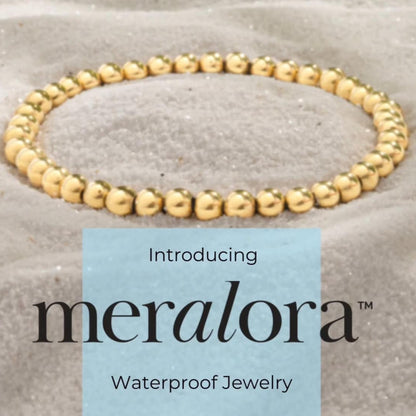 Gold beaded bracelet on a textured surface with 'meralora' branding.