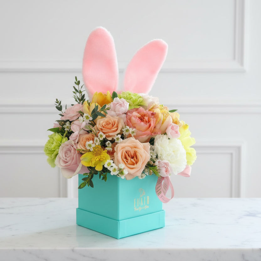 Floral arrangement in a box with bunny ears on a white surface