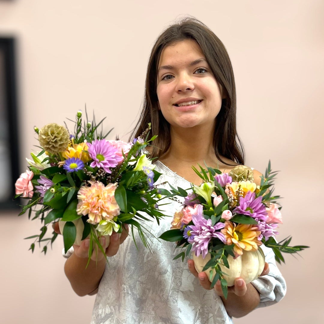 A woman holding two small floral arrangements with pastel flowers and greenery, workshop at Flair Flower Bar.