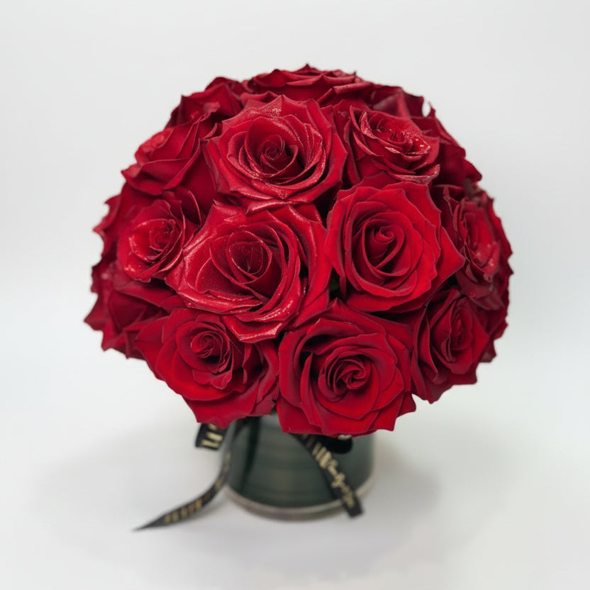 A dense bouquet of deep red roses arranged in a clear vase on a white surface, designed by Flair Flower Bar & Studio in Florence, Kentucky with Delivery in Cincinnati and Northern Kentucky