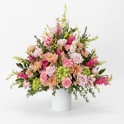 Funeral arrangement of pink, green, and white flowers in a white vase on a white background