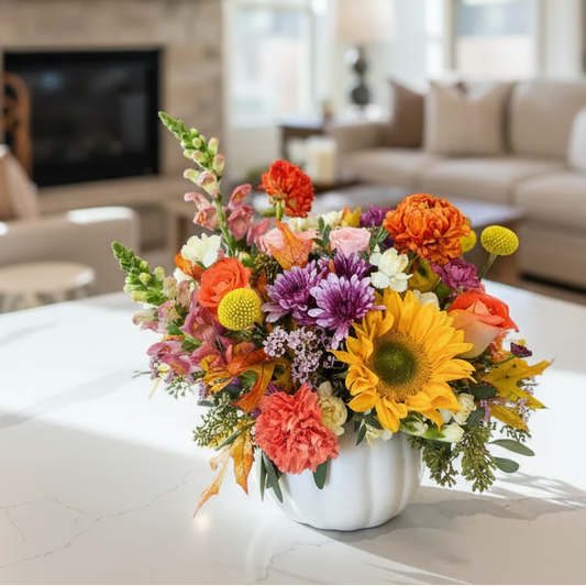 Colorful fall flower arrangement in a white pumpkin vase on a coffee table in a living room.