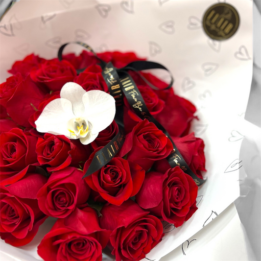 Bouquet of red roses with a white orchid and black ribbon in a box