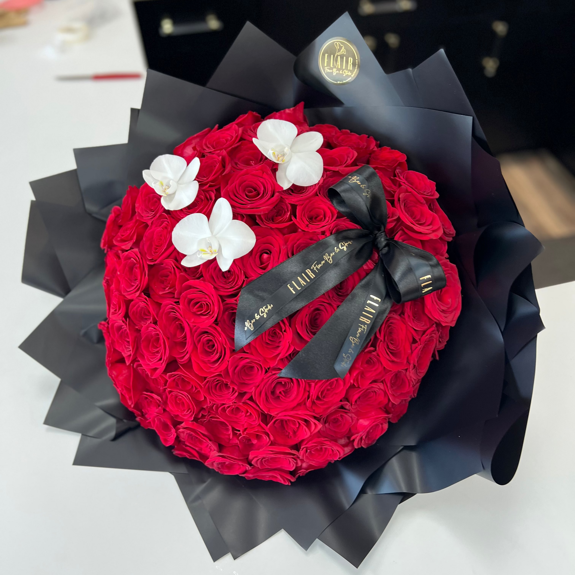 100 Red rose bouquet with black ribbons and white flowers on a white surface