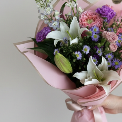 Bouquet of flowers wrapped in pink paper held by a hand on a light gray background