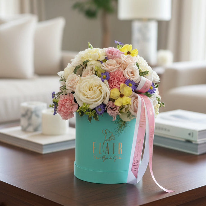 A vibrant floral arrangement in a turquoise cylindrical box with a pink ribbon, displaying the gold 'FLAIR' logo in Cincinnati home