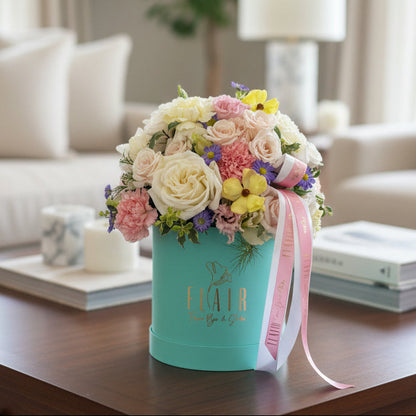 A vibrant floral arrangement in a turquoise cylindrical box with a pink ribbon, displaying the gold 'FLAIR' logo in Cincinnati home