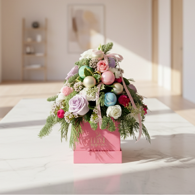 Decorative christmas floral arrangement with colorful ornaments in a pink box on a white surface.