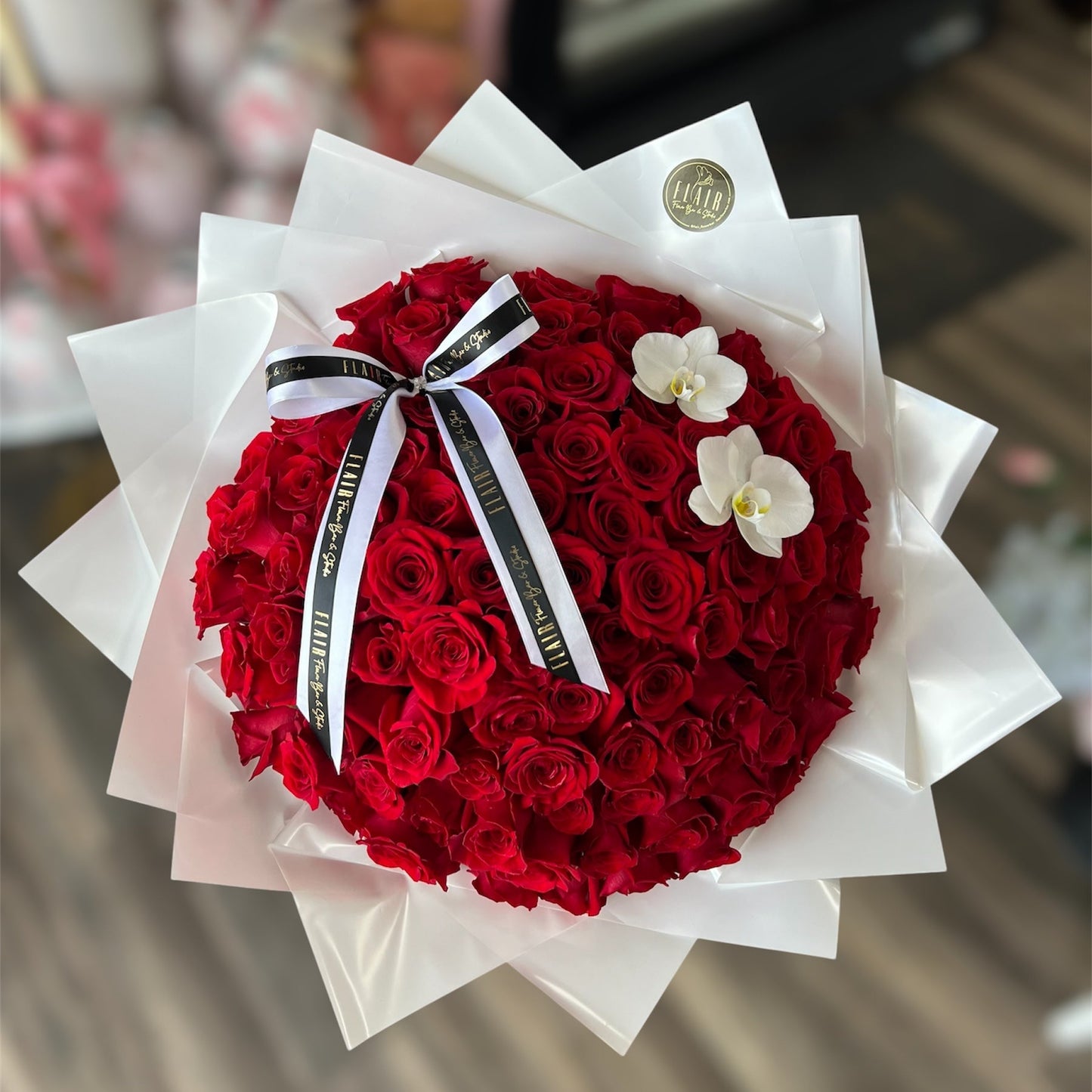Bouquet of red roses with a white ribbon and orchids, wrapped in white paper.