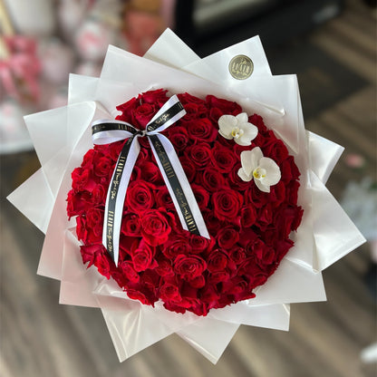 Bouquet of red roses with a white ribbon and orchids, wrapped in white paper.