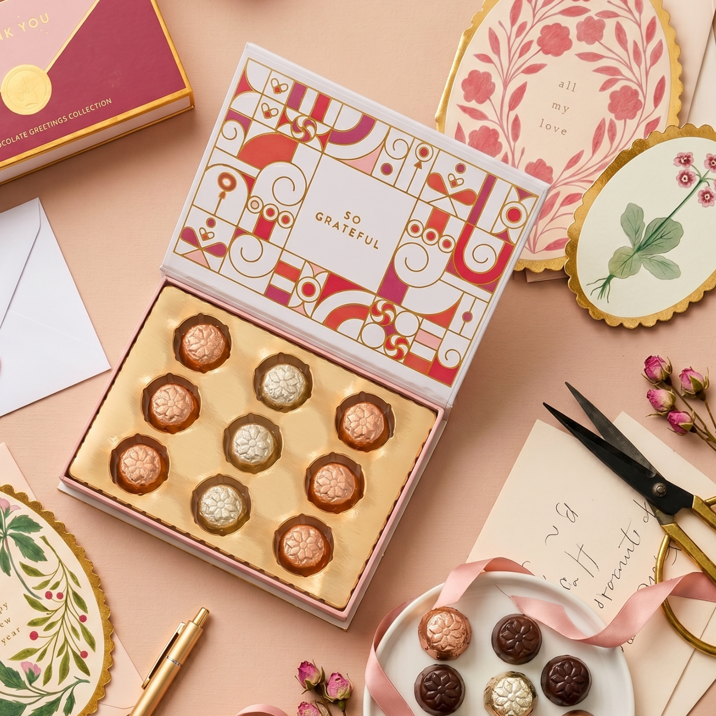 Decorative box of chocolates with a pink and gold theme on a matching surface.