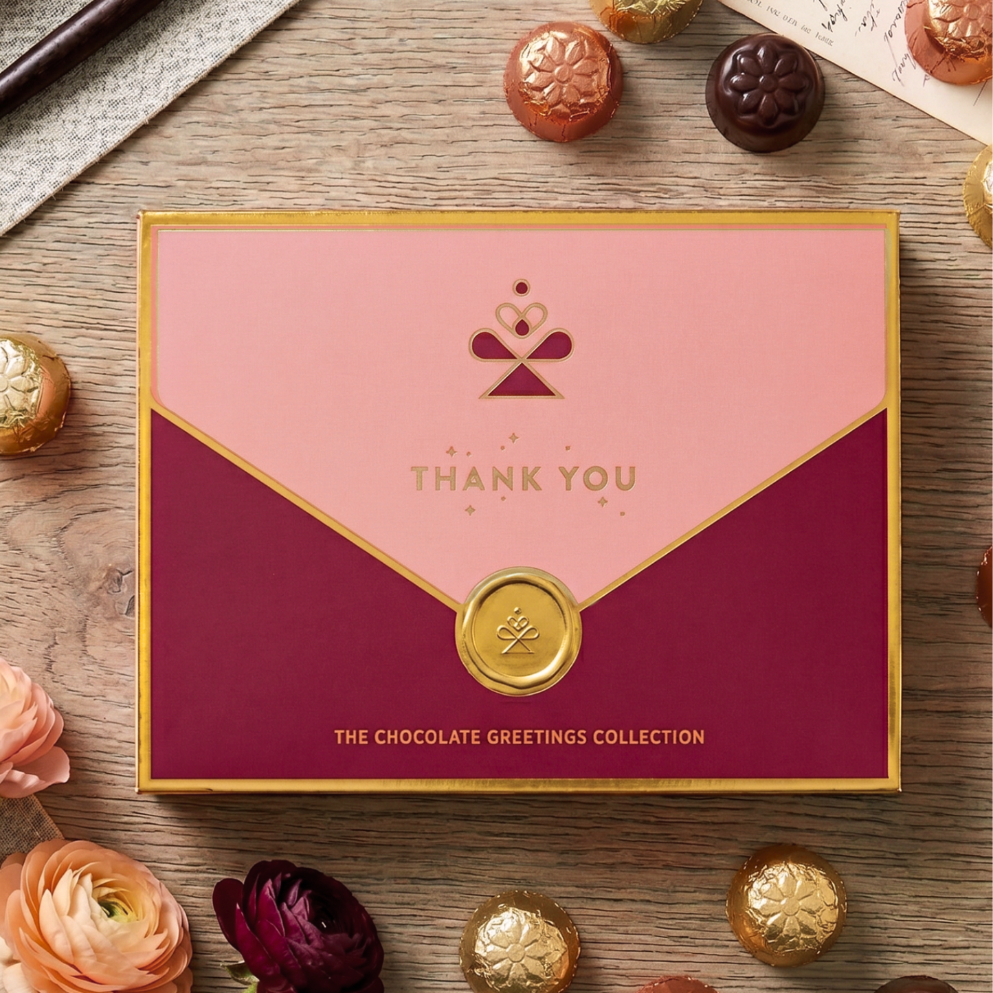 Pink and red gift box with 'Thank You' text on a wooden surface with chocolates and flowers.