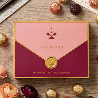 Pink and red gift box with 'Thank You' text on a wooden surface with chocolates and flowers.