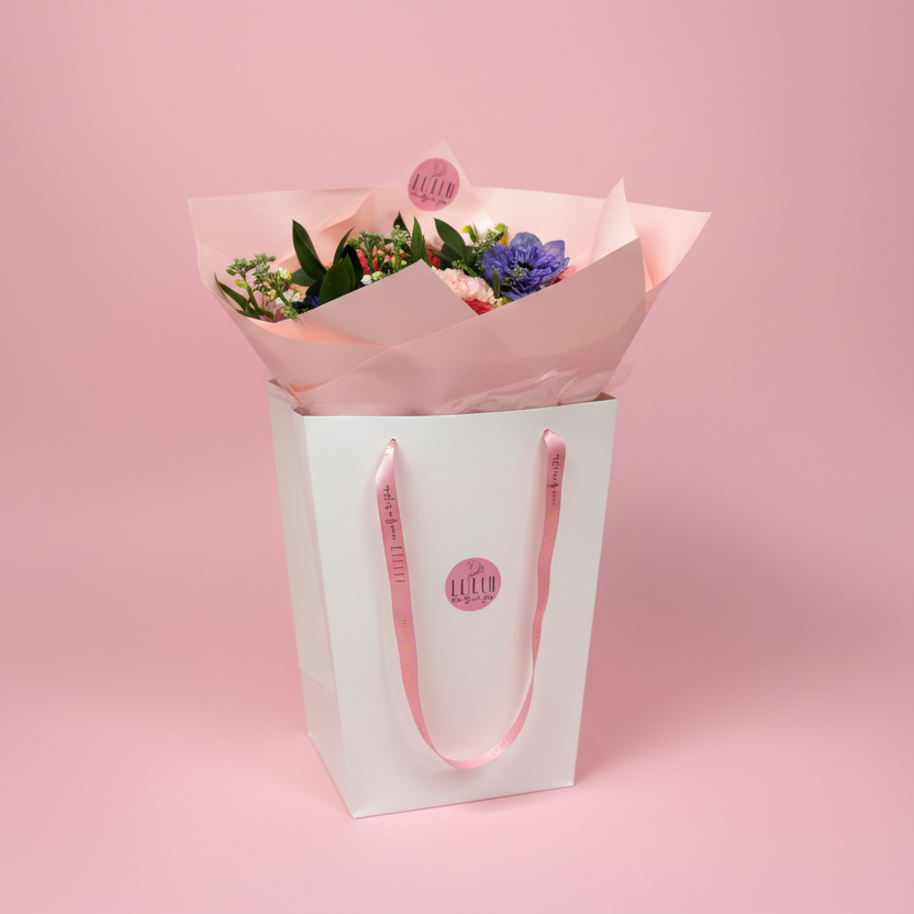 Bouquet of flowers wrapped in pink paper with a white box on a blurred pink background-Cincinnati Flower Delivery