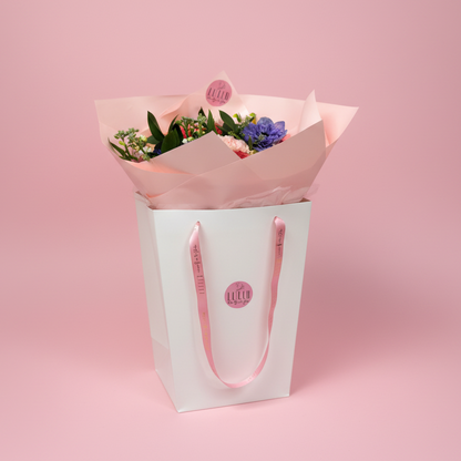 Bouquet of flowers wrapped in pink paper with a white box on a blurred pink background-Cincinnati Flower Delivery