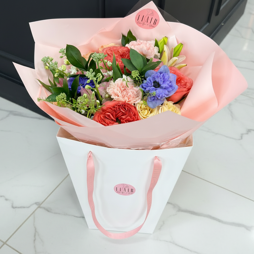 Bouquet of flowers in a white bag with pink accents on a marble floor.