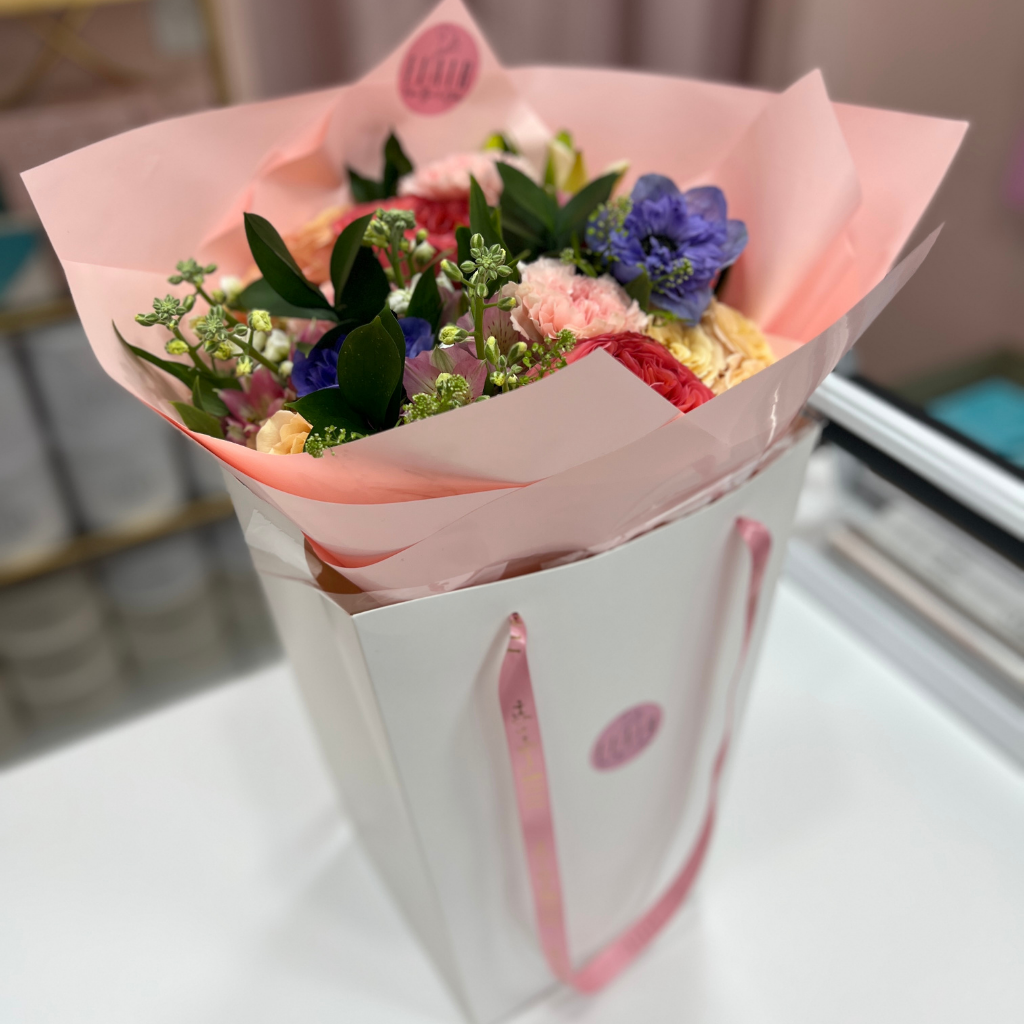 Bouquet of flowers wrapped in pink paper with a white box on a blurred background