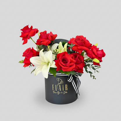 Floral arrangement with red roses and white lilies in a black box labeled 'Flair'.