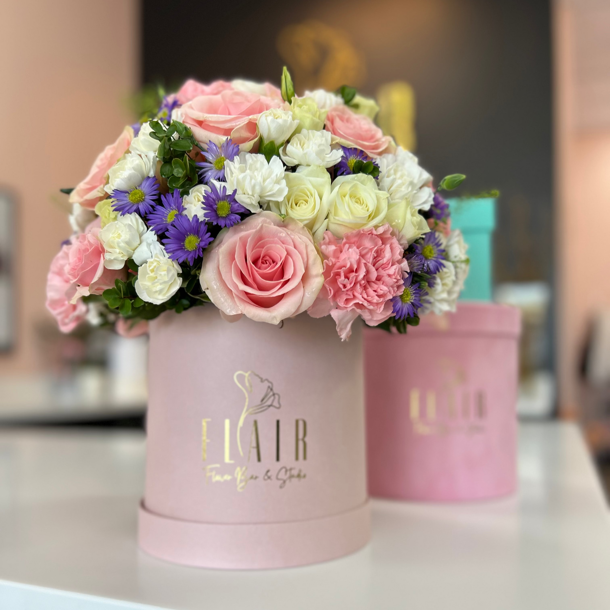 Floral arrangement in a pink box with 'FLAIR' branding on a blurred background