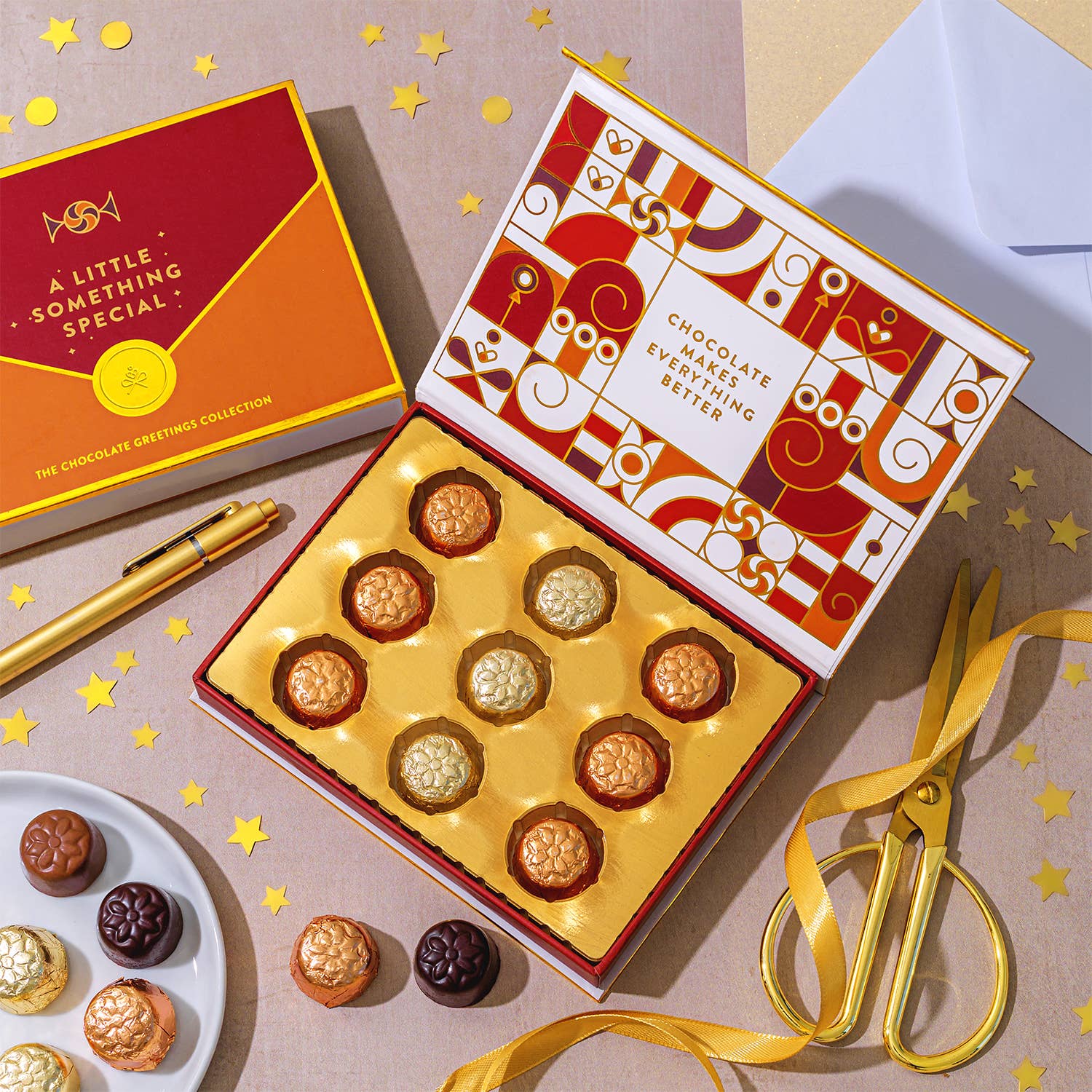 Box of chocolates with decorative packaging on a table with gold ribbon and scissors.
