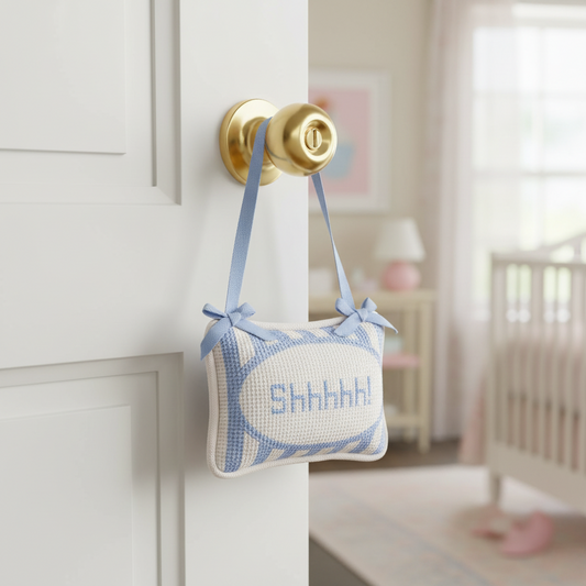 Decorative pillow with 'SHH' text attached to a door handle in a nursery setting.