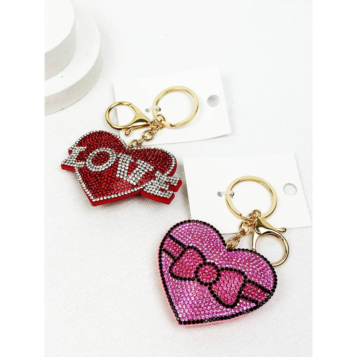 Two heart-shaped keychains, one red with 'LOVE' and the other pink with a bow design, on a white background.