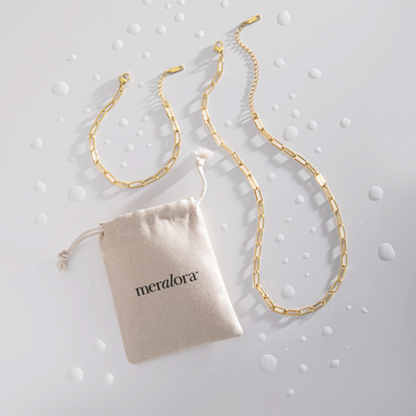 Gold chain necklace with a 'meralora' branded pouch on a textured gray background
