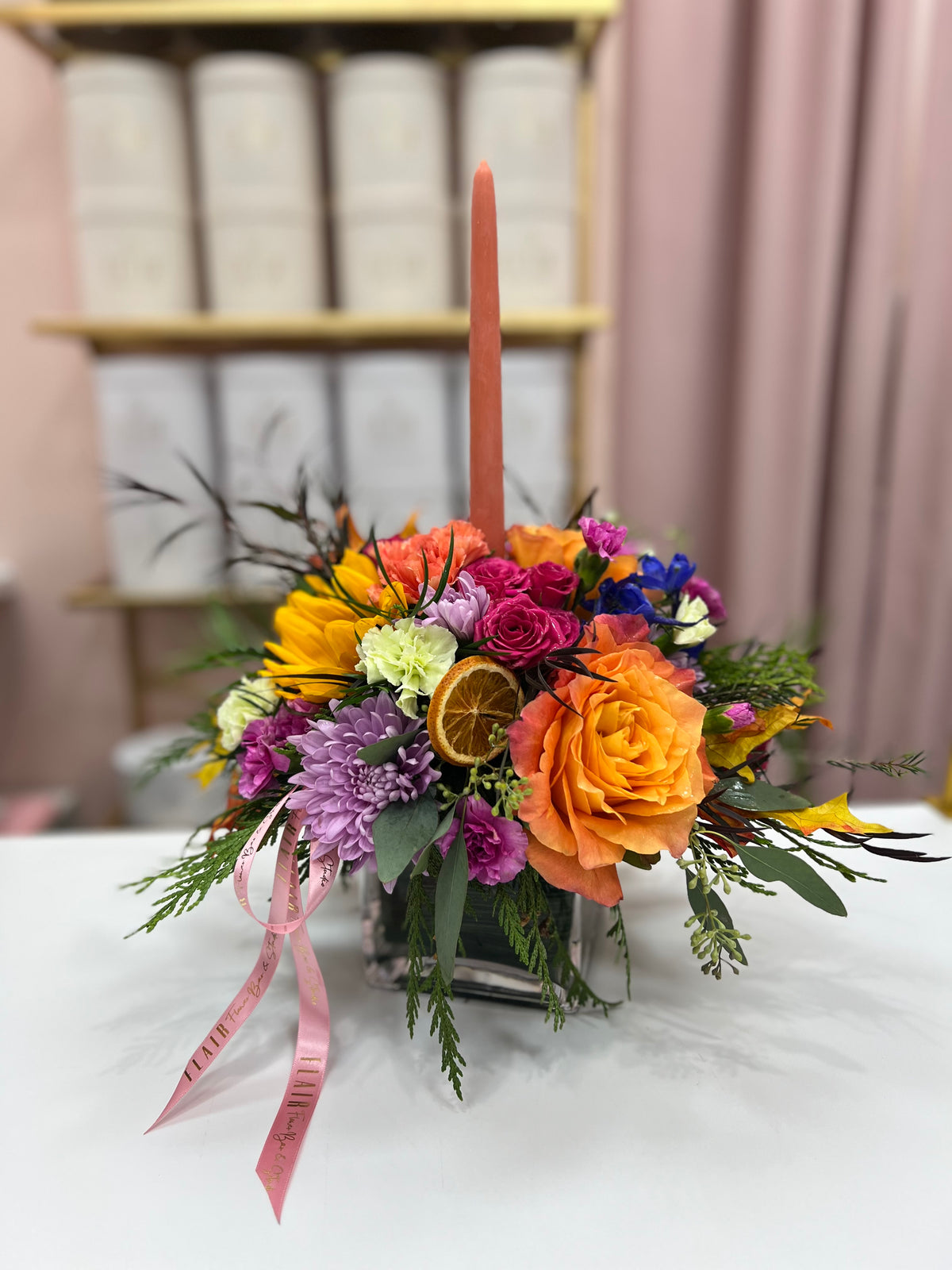 Fall centerpiece in a square glass vase with orange taper candle, orange and pink roses, and purple flowers, Cincinnati florist